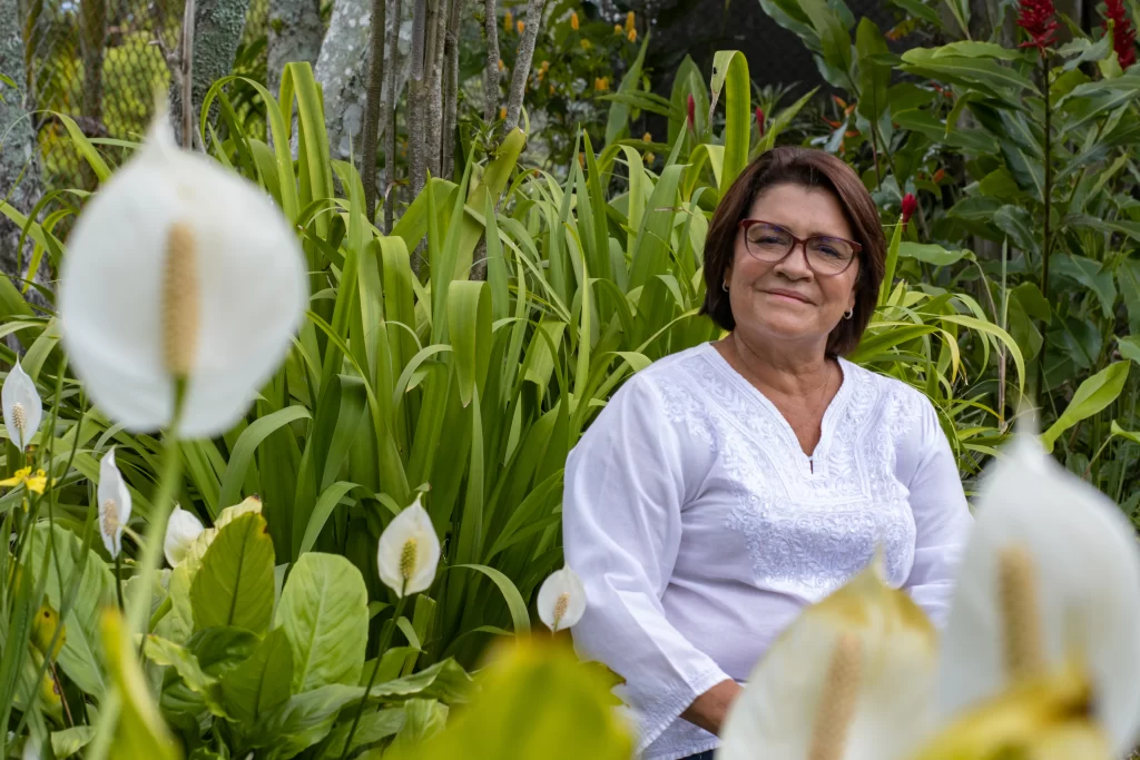 Dra. Leda Ureña Umaña, fundadora de Psiconstelar, sonriendo en un jardín rodeada de flores blancas y naturaleza.